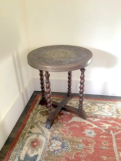 a small wooden table sitting on top of a red rug next to a white wall