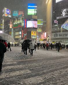 people walking in the snow with umbrellas on a busy city street at night time