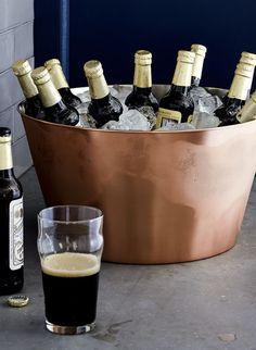 a large metal bucket filled with bottles of beer next to a glass and bottle opener