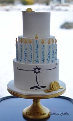 a three tiered cake with lit candles on the top and writing on the side