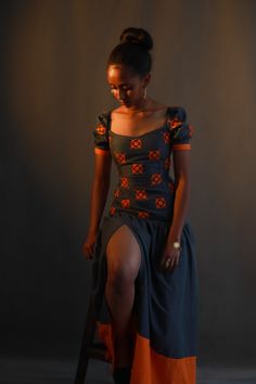 a woman sitting on a stool in a dress with an orange and black pattern, posing for the camera