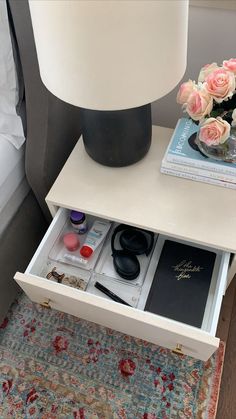 a white nightstand with drawers and flowers on the side table next to a lamp in a bedroom