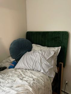 an unmade bed with white sheets and green headboard in a small corner room