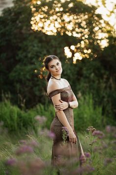 a woman is standing in the grass with her arms around her chest and looking at the camera