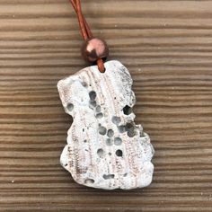 a white piece of rock with holes in it on a brown leather cord that is sitting on a wooden surface