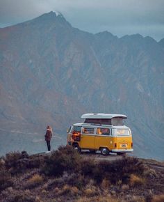 a yellow and white vw bus parked on top of a hill next to a person