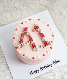 a pink birthday cake decorated with flowers and the letter h on it's side