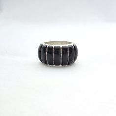 This stylish Sanel Native American Navajo artisan crafted sterling silver ring has 7 pieces of natural onyx stone inlaid into the band creating a striking design that seems to be a signature design for Sanel. Hallmarked Sanel with 925 on the inside of the ring (see photograph). Size: 9 Width at widest: 1/2" The condition is good for having been previously owned.  There are small light marks visible on the flat areas of the sterling and some buff marks on some of the onyx stones. I believe these can be polished away. Shipping is only to US addresses at this time and via USPS Ground Advantage. You will be provided a tracking number and an estimated date of delivery. **Shipping is upgraded to Priority Mail when 2 or more items are combined or order exceeds $75.** PLEASE NOTE: Please read the Black Artisan Jewelry With Polished Finish, Artisan Black Jewelry With Polished Finish, Artisan Black Sterling Silver Rings, Black Inlay Round Ring, Artisan Black Round Ring, Black Sterling Silver Jewelry With Inlay, Black Ring With Inlay, Black Rings With Inlay, Southwestern Black Sterling Silver Jewelry