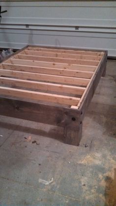 a wooden bed frame sitting on top of a floor next to a white garage door