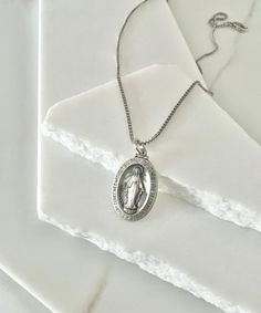 "✨ Discover divine elegance with our Sterling Silver Miraculous Mary Pendant. Crafted with exquisite detail, this 28mm oval pendant features an antiqued Virgin Mary, radiating timeless grace and spiritual significance. The intricately designed pendant is a symbol of faith, protection, and devotion. Made of sterling silver, it boasts enduring quality and beauty. Complete your ensemble with the optional 1.3mm box necklace, crafted from the same sterling silver for a seamless look. Whether worn for Classic Antique Silver Oval Necklace, Classic Oval Antique Silver Necklace, Classic Oval Jewelry With Oxidized Finish, Oval Silver Necklace With Antique Finish, Box Necklace, First Communion Gifts, Necklace Men, Necklace Box, Delicate Details