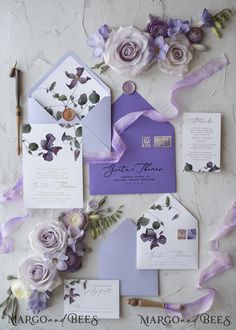 purple and white wedding stationery with flowers on the side, including lettered envelopes