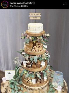 a three tiered cake sitting on top of a wooden table covered in greenery