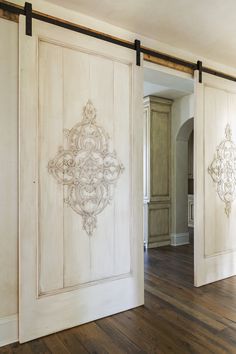 an open door in a room with wood flooring and white painted doors that have intricate designs on them