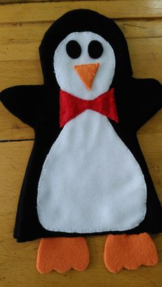 a felt penguin with a red bow on it's head and legs sitting on a wooden floor