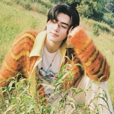 a young man sitting in the grass with his hand on his head and wearing a striped jacket