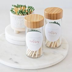 two jars with matches and some plants in them on a marble tray next to each other