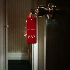 a red room number sign hanging from the side of a door with a hallway in the background