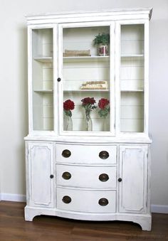 a white china cabinet with flowers in vases