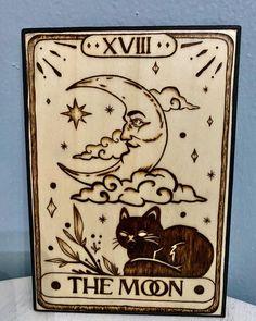 a wooden plaque with an image of a cat and the moon on it's side