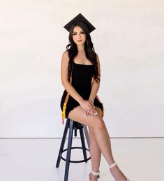 a woman sitting on top of a stool wearing a graduation cap