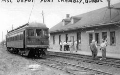 black and white photograph of people standing on the tracks next to a train