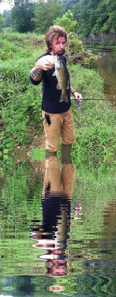 a man holding a fish in his hands while standing on the side of a body of water