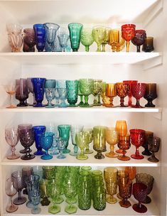 a shelf filled with lots of different colored glasses on top of white shelve