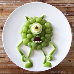 a white plate topped with grapes and a green monster made to look like it's smiling