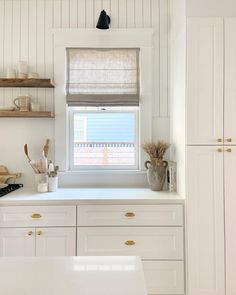 a kitchen with white cabinets and open shelves on the wall, along with a window covered in blinds