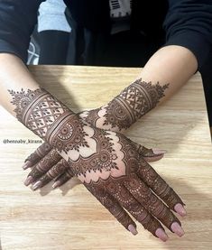 the hands are decorated with henna designs on top of a wooden table in front of a woman's face