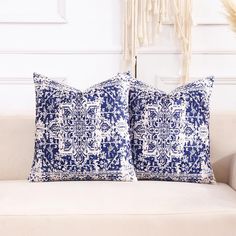 two blue and white pillows sitting on top of a couch next to a wall hanging