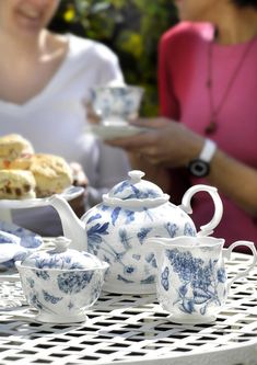 two women sitting at a table with blue and white teapots, cups and saucers