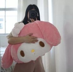 a woman holding a large hello kitty stuffed animal in front of her face while taking a selfie