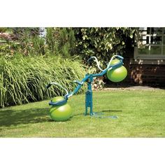 two green and blue balls are in the grass next to a metal pole with an upside down ball on it