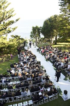 an outdoor ceremony with rows of chairs and people walking down the aisle in front of them