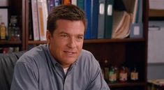 a man sitting at a desk in front of a book shelf with books on it