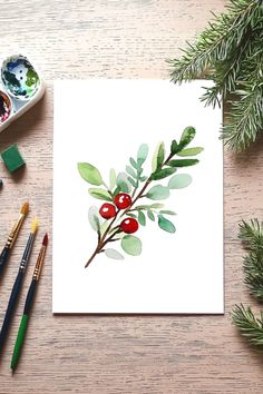 A simple winter watercolor greenery painting featuring green leaves and red berries, surrounded by brushes and pine branches. Winter Berries Watercolor, Cute Christmas Watercolor Paintings, Hand Painted Christmas Cards Ideas, Watercolor Christmas Art Simple, Watercolor Christmas Flowers, Christmas Painted Cards, Watercolor Painting Cards, Easy Watercolor Paintings Christmas, Holiday Watercolor Ideas