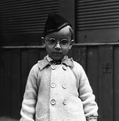 black and white photograph of a young boy wearing glasses, a jacket with buttons on it