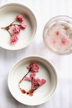 two white plates with pink flowers on them next to a glass filled with ice and water