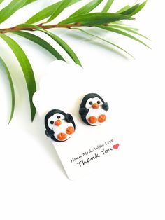 penguin earrings with thank you written on the front and back, sitting next to a green leaf