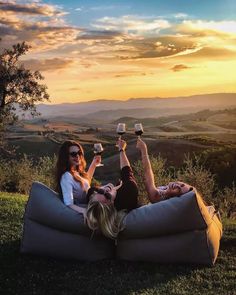 two women sitting on a bean bag chair with wine glasses in their hands and the sun setting behind them