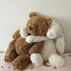 two brown and white teddy bears hugging each other on a pink surface with gold stars