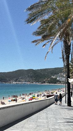 people are walking along the beach with palm trees and blue water in the back ground