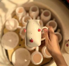 a person is holding a white vase with red berries on it and some cups in the background