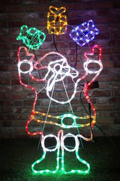 an outdoor christmas decoration with lights and decorations on the grass in front of a brick wall