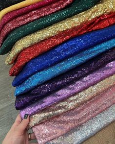 several colors of sequin fabric are stacked on top of each other, with one hand holding