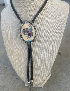 This awesome bolo tie has a vintage cowboy print with a clear resin coating and metal backing. Handmade in our shop! The cord is black and genuine leather. Our bolos pair nicely with many of our belt buckles! They make wonderful gifts.    The western bolo tie rope length is 39' ;  pendant size is 1 1/2'' x 1 1/4'' Cowboy Jewelry Men, Bolo Tie Tattoo, Bolo Tie Outfit, Cowboy Necktie, Cowboy Tie, Cowboy Suit, Bolo Tie Men, Cowboy Jewelry, Western Bolo Tie