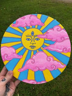 a hand holding up a painted frisbee with a sun and clouds on it