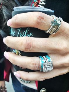 a woman's hand with several rings on it and a phone in her other hand