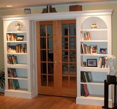 a living room filled with lots of white bookshelves and wooden floors next to a doorway